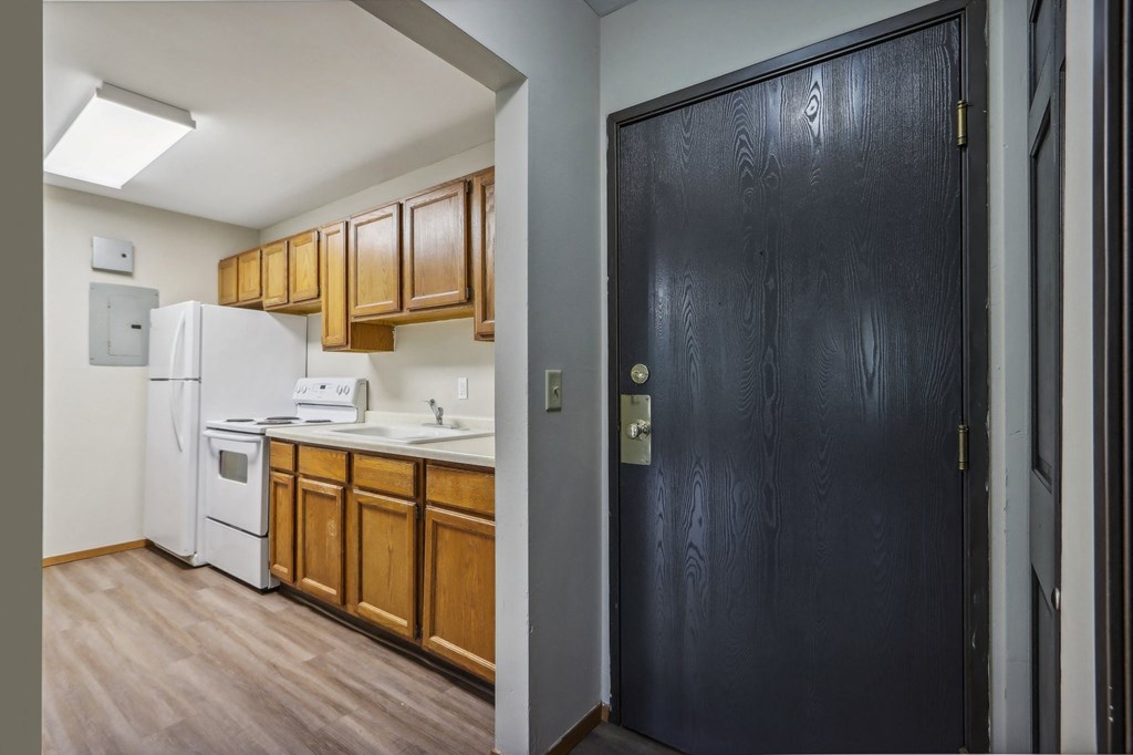 a kitchen with wooden cabinets and white appliances and a black door
