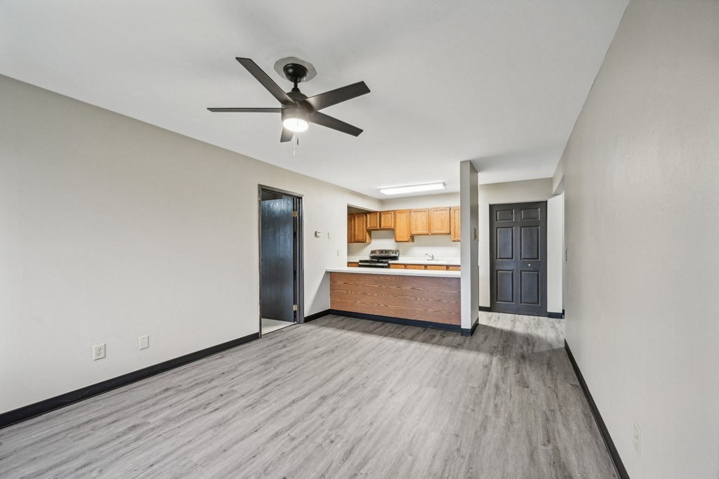 an empty living room with a ceiling fan and a kitchen