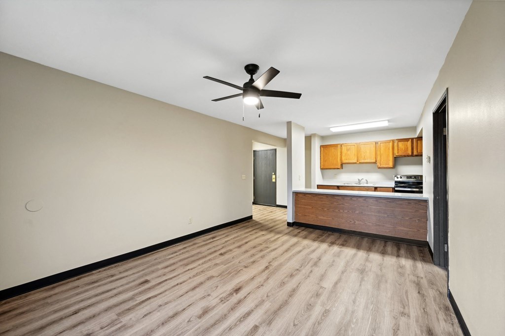 a empty living room with a ceiling fan and a kitchen