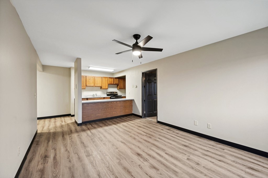 a empty living room with a ceiling fan and a kitchen