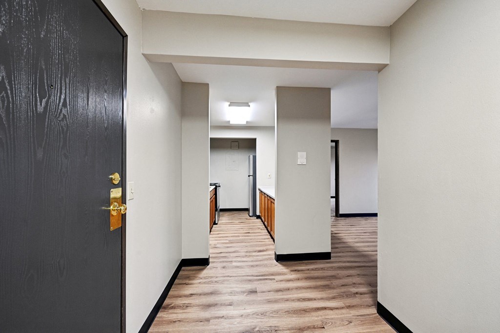 an empty hallway with a black door and white walls and wood floors