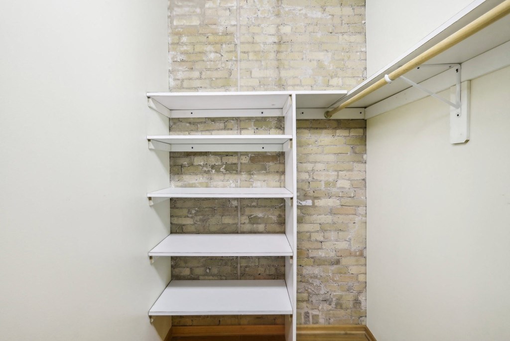 a walk in closet with white shelves and brick walls