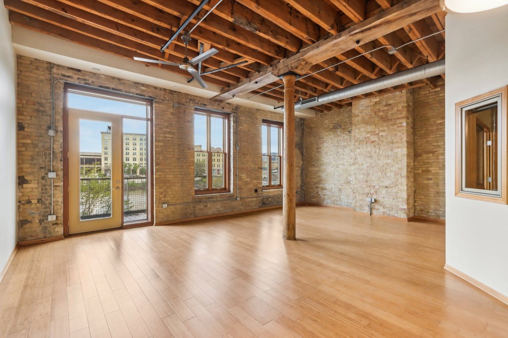 an empty living room with exposed brick walls and wood floors