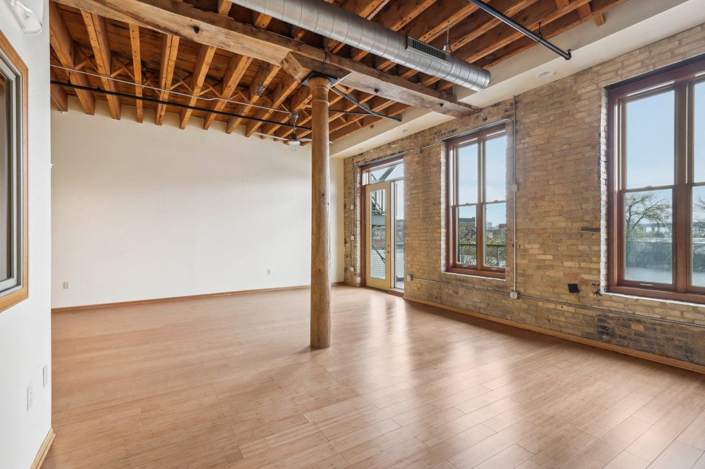 an empty room with wood floors and a brick wall and large windows