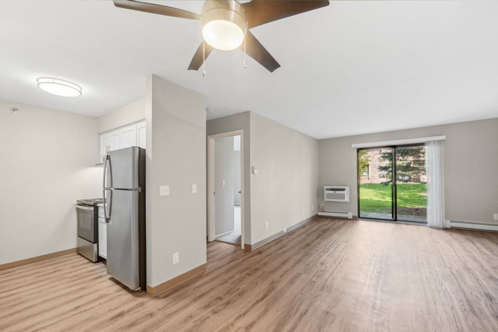 an empty living room with a refrigerator and a ceiling fan