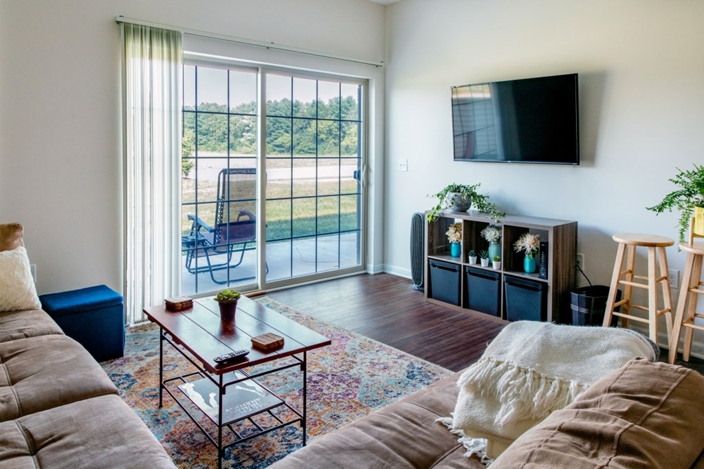 A living room with a couch, a coffee table, a TV, and a window with a view of the outside.