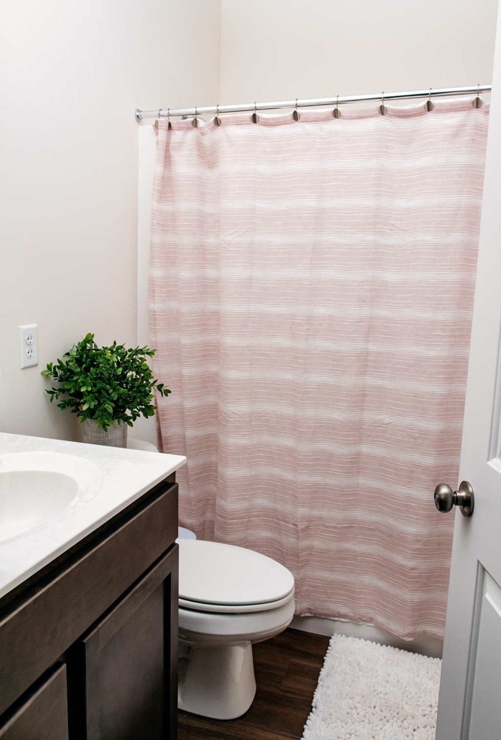 A white toilet sits under a pink shower curtain in a bathroom.