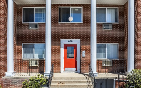A red door is the centerpiece of a brick building with white columns.