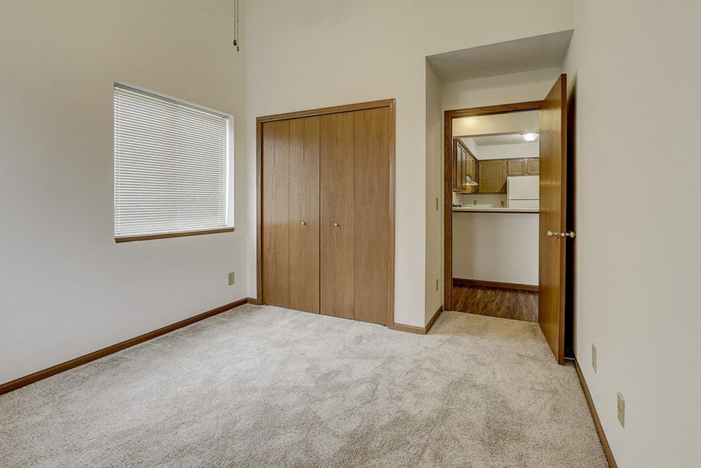 an empty living room with carpet and a door to a kitchen