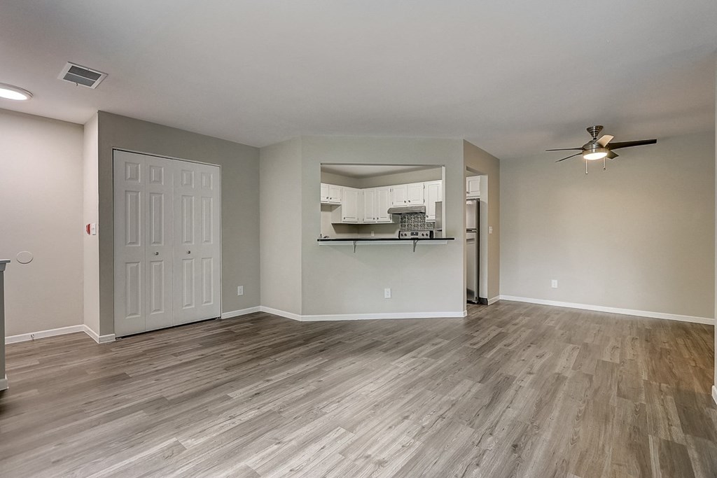 an empty living room with a kitchen in the background