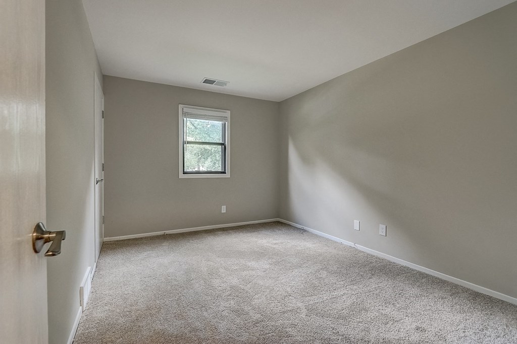 an empty bedroom with white carpet and a window