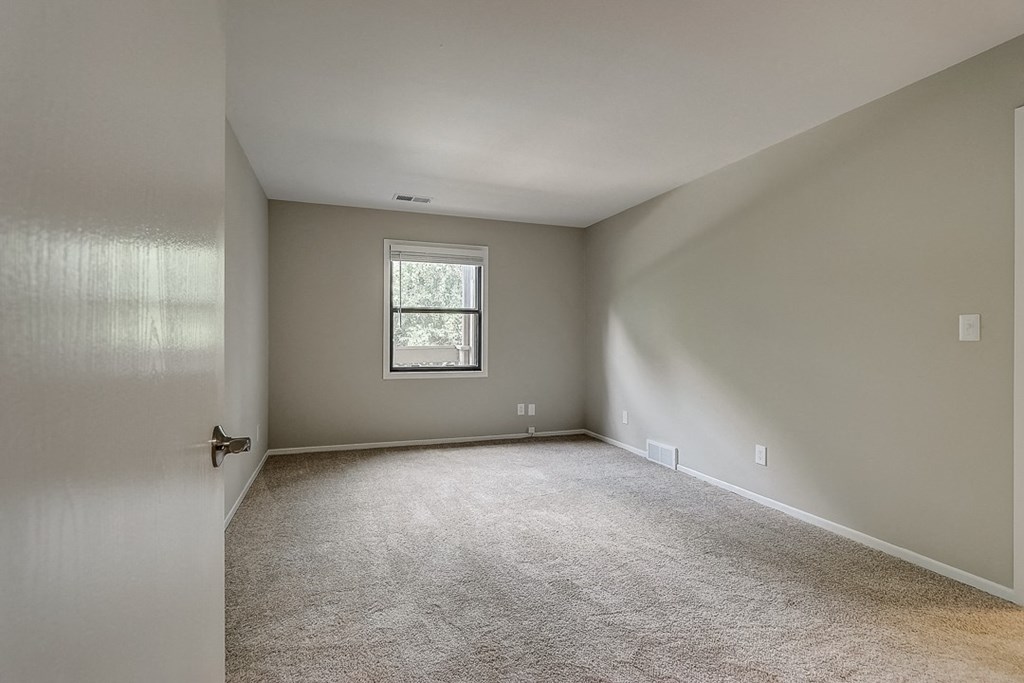 an empty bedroom with white carpet and a window