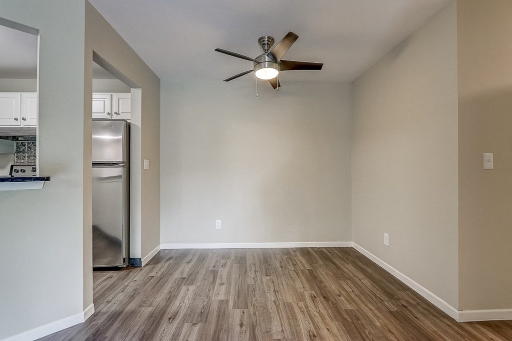 an empty living room with a ceiling fan and a kitchen