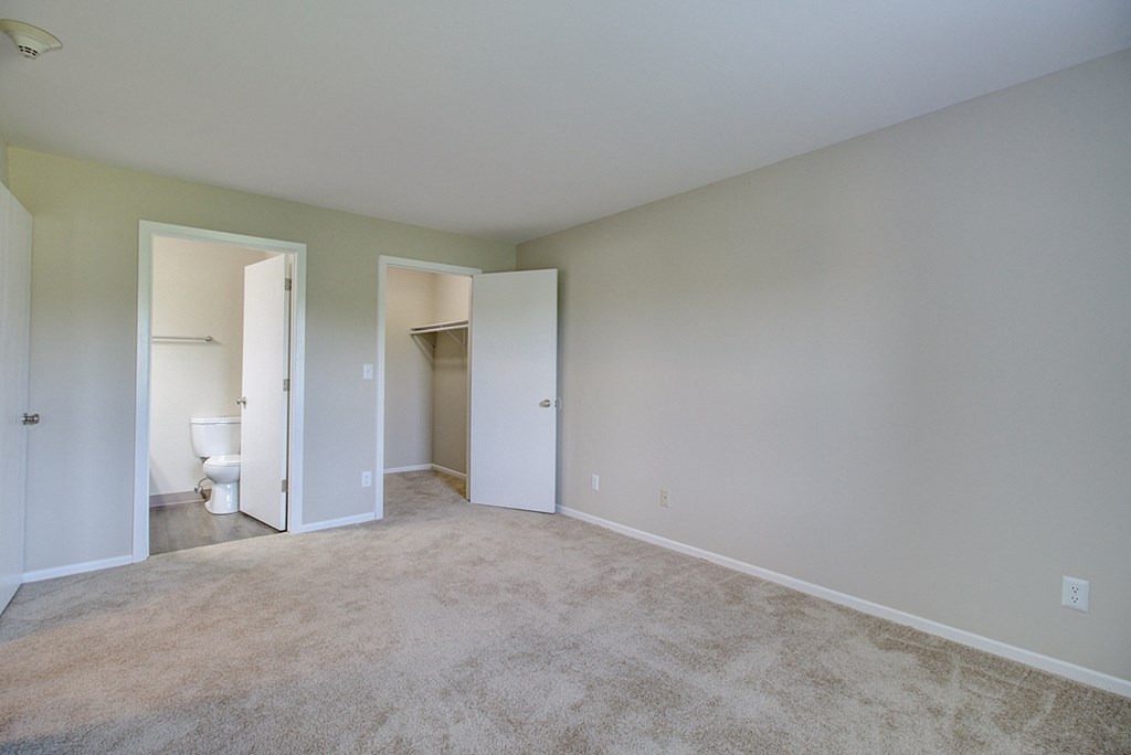an empty living room with a carpeted floor and a door to a bathroom