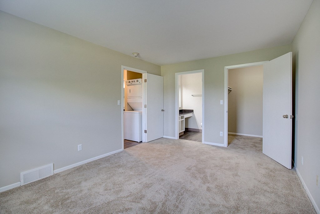 an empty living room with a carpeted floor and a door to a bathroom