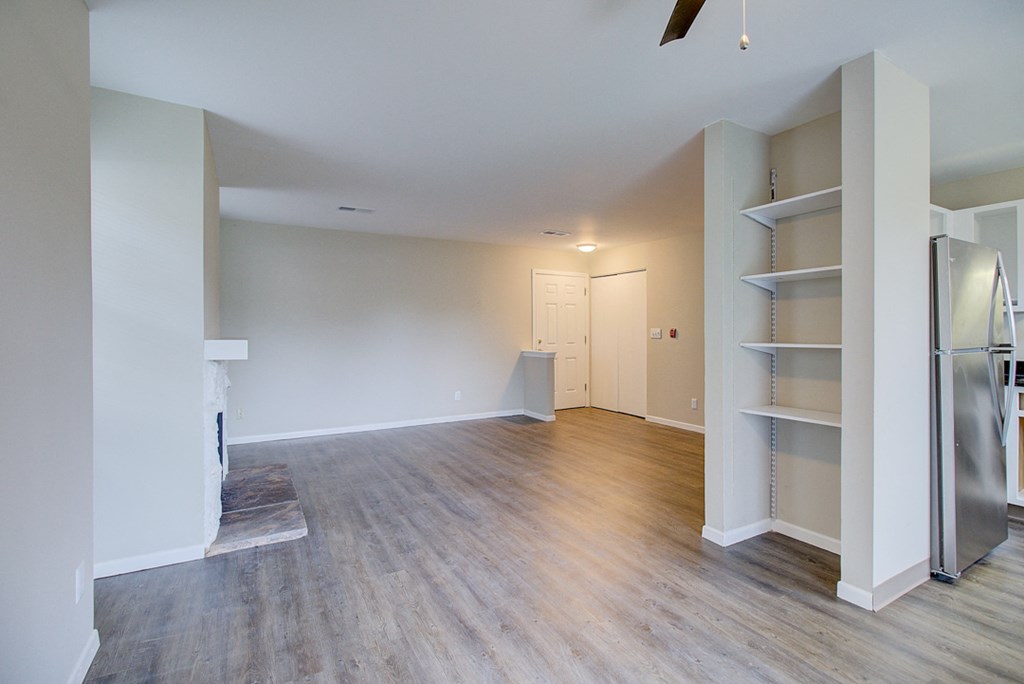an empty living room with wood flooring and a stainless steel refrigerator