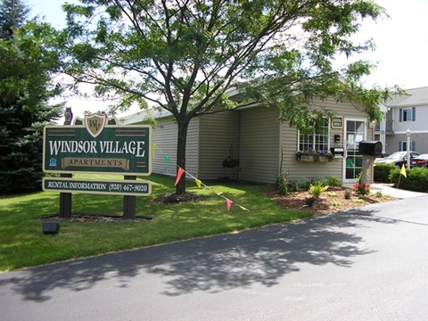 A sign for Windsor Village Apartments is in front of a building.