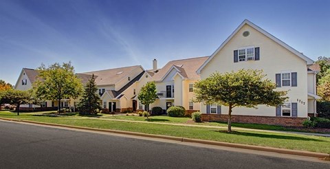 A white house with a brown roof and a tree in front of it.