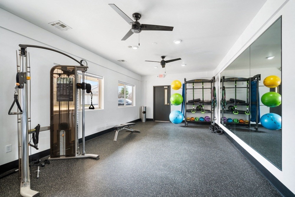 a gym with weights and mirrors and a ceiling fan