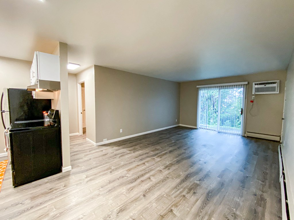 an empty living room with a kitchen and a sliding glass door