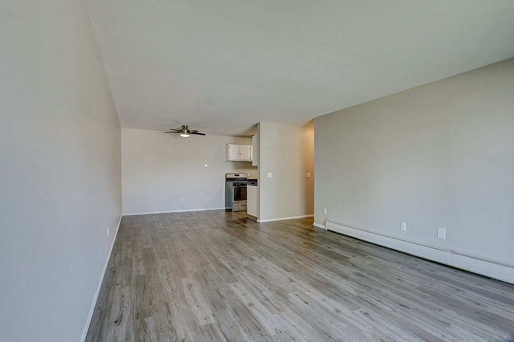 an empty living room with wood flooring and a kitchen