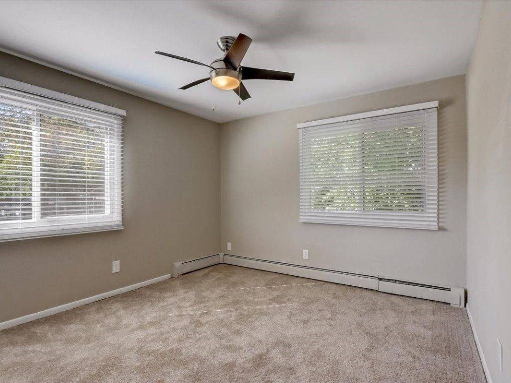 an empty bedroom with a ceiling fan and two windows