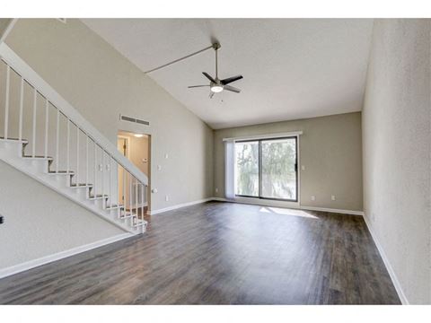 an empty living room with a staircase and a ceiling fan