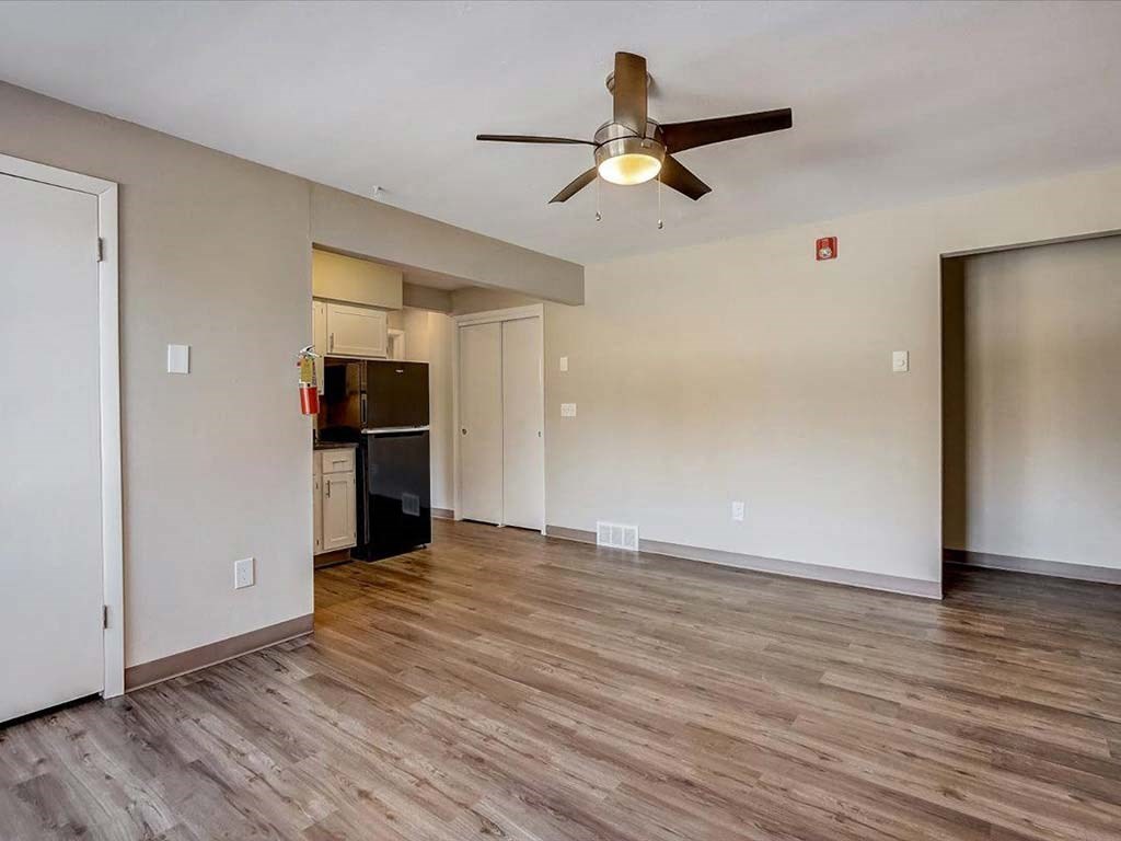 an empty living room with a ceiling fan and a kitchen