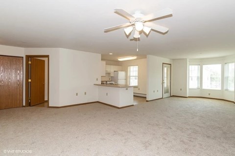 A spacious living room with a ceiling fan and carpeted floor.