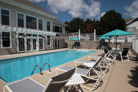 A pool with chairs and umbrellas in front of a house.