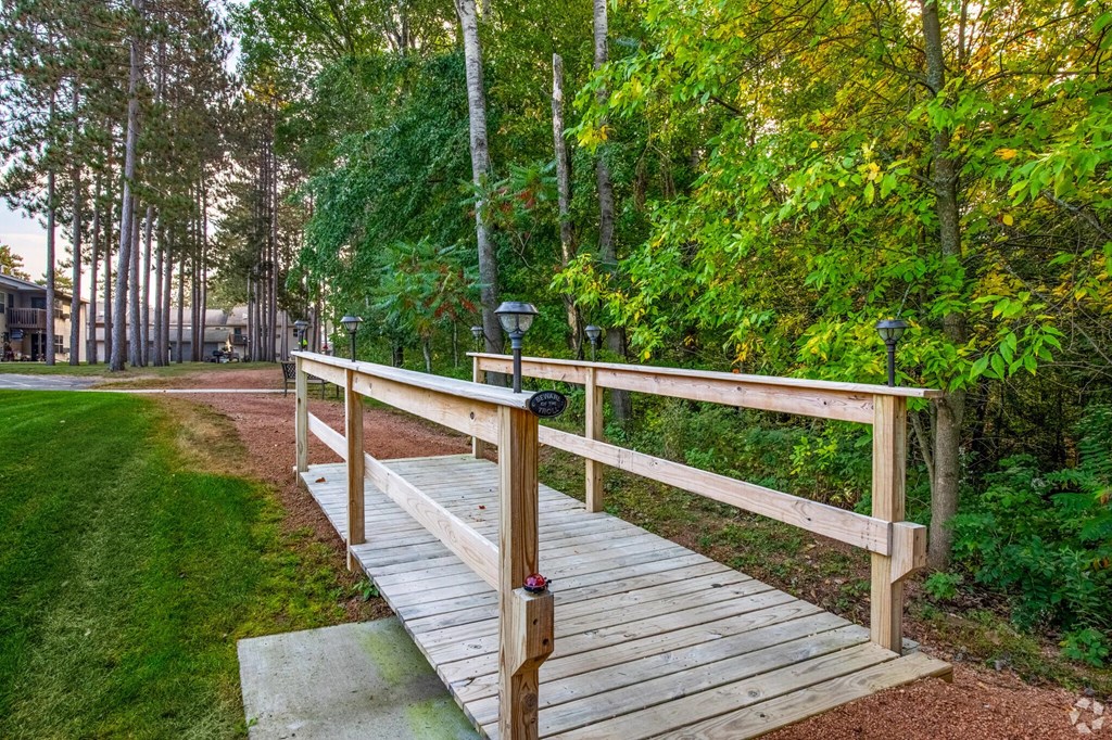 A wooden bridge over a grassy area with trees in the background.