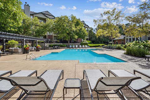 A pool surrounded by lounge chairs and trees.