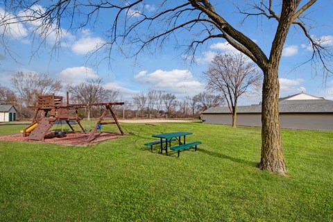 A playground with a green picnic table and a wooden swing set.