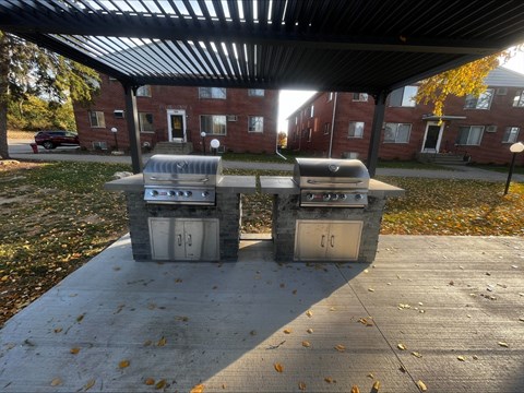 Two trash cans are placed under a shelter on a sidewalk.