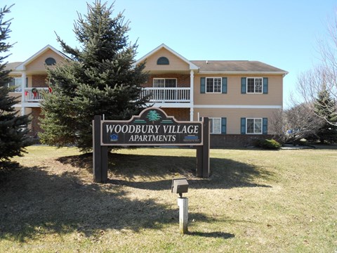 A sign for Woodbury Village Apartments stands in front of a building.