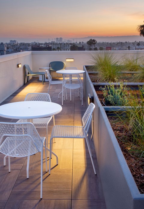 A patio with a table and chairs overlooking a cityscape at sunset.