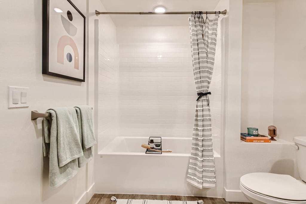 a bathroom with a white toilet next to a bathtub with a shower curtain at The Venue at Orange Apartments, California