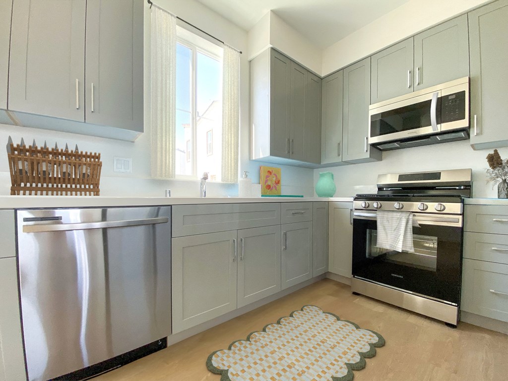 a kitchen with stainless steel appliances and gray cabinets at The Willow Townhomes, Ontario, CA