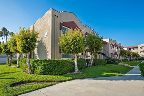 A building with a beige exterior and a red roof is surrounded by greenery.