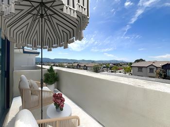 a balcony with a table and chairs and an umbrella at The Max on Jefferson Apartments, Murrieta, California