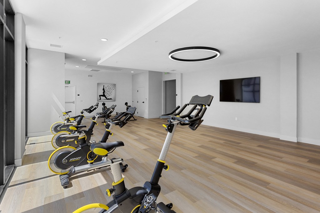 a gym with rows of exercise bikes and a tv on the wall at The Venue at Orange Apartments, Redlands, 92373