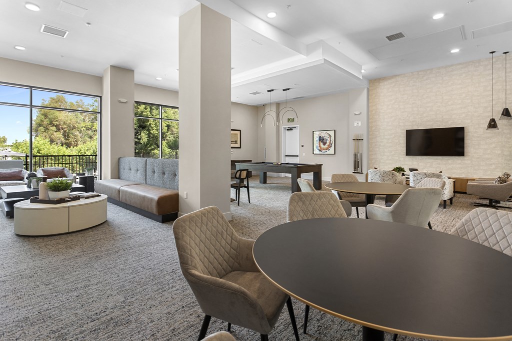 a clubhouse with couches tables and chairs and a television at The Venue at Orange Apartments, Redlands, California