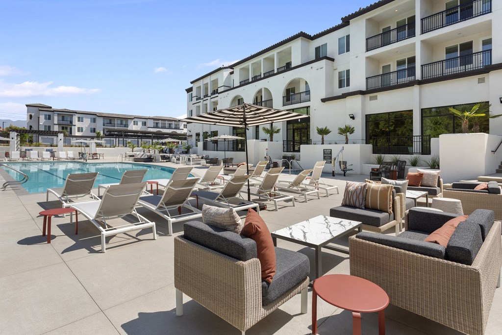 a person sitting on a lounge chair next to a pool at The Venue at Orange Apartments, Redlands, CA