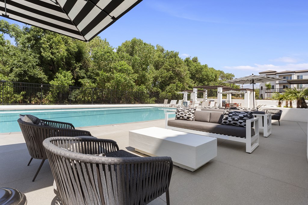 a poolside patio with chairs and tables and a pool at The Venue at Orange Apartments, Redlands