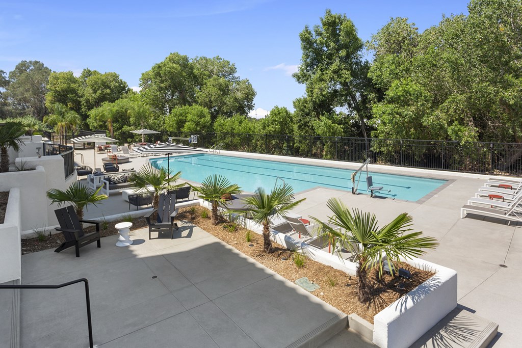 a swimming pool with tables and chairs and trees in the background at The Venue at Orange Apartments, Redlands, California