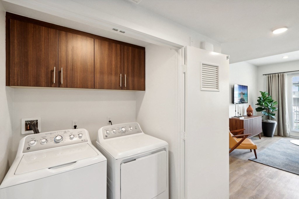 a washer and dryer in a laundry room with a living room and kitchen at The Max on Jefferson Apartments, California, 92562