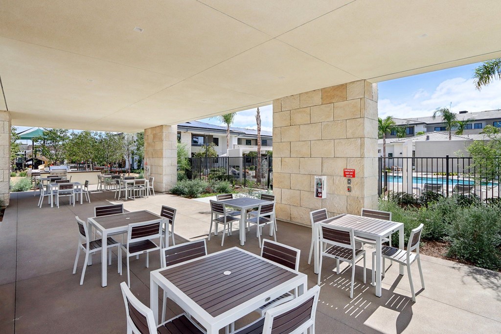a patio with tables and chairs and a pool in the background at The Max on Jefferson Apartments, California