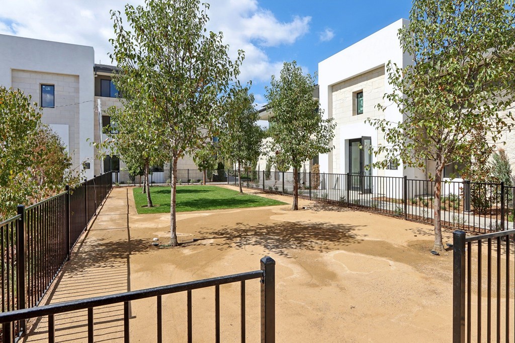 a courtyard with trees and a fence and apartments in the background at The Max on Jefferson Apartments, Murrieta