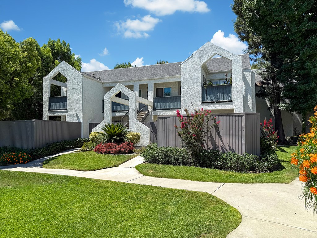 A white house with a grey roof and a green lawn in front at Ridgeline Apartments in San Bernardino