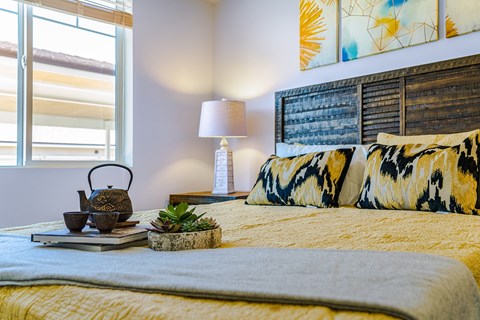 A bed with a yellow comforter and a small potted plant on a tray.